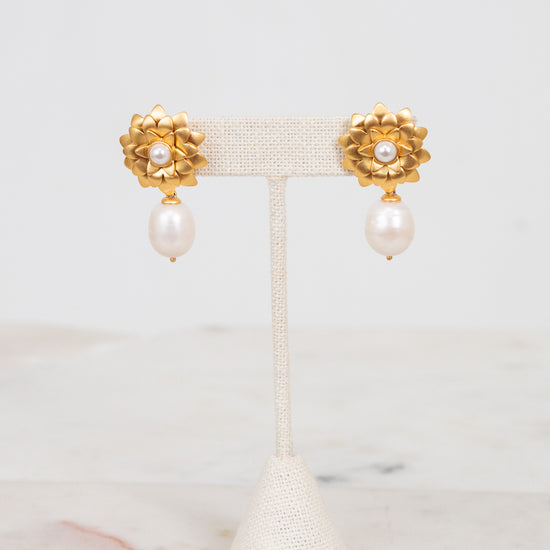 Pair of gold earrings with pearl drops on a white stand against a light background