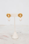 Pair of gold earrings with pearl drops on a white stand against a light background