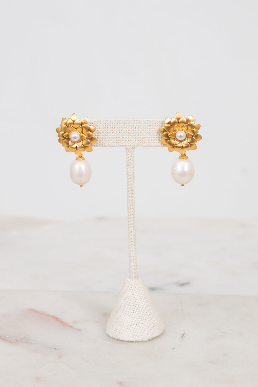 Pair of gold earrings with pearl drops on a white stand against a light background