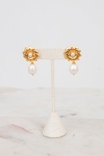 Pair of gold earrings with pearl drops on a white stand against a light background