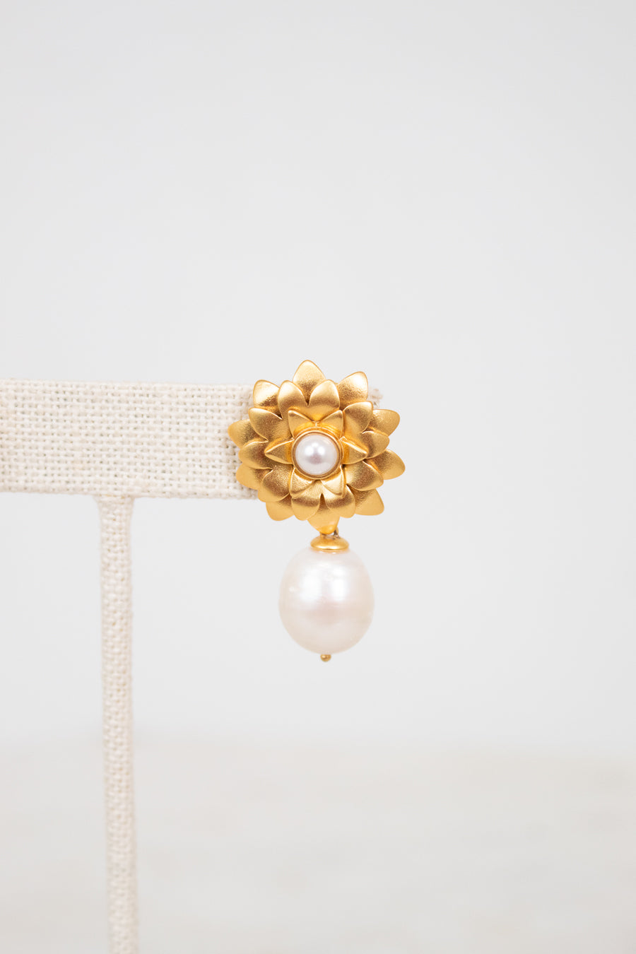 Gold earring with pearl on a light gray background