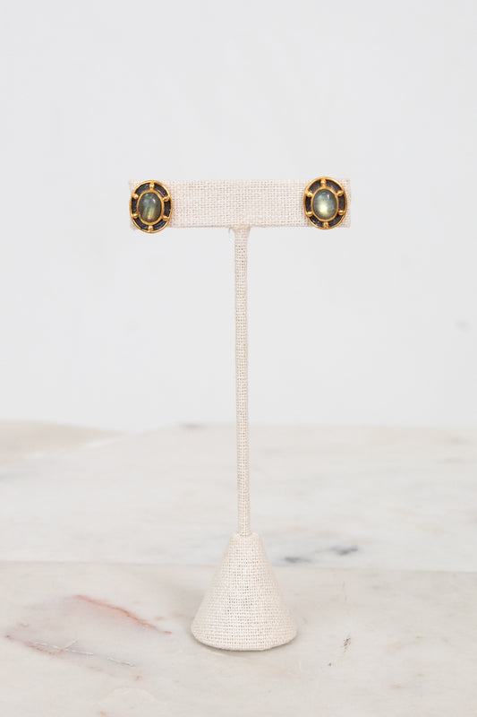 Pair of gold earrings on a white stand with a marble background