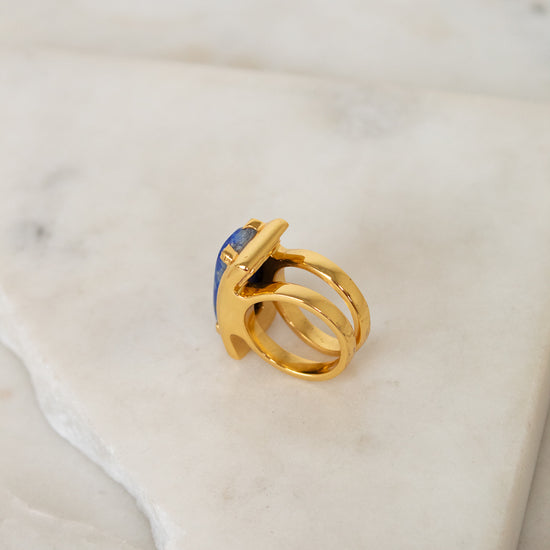 Gold ring with a blue gemstone on a marble surface