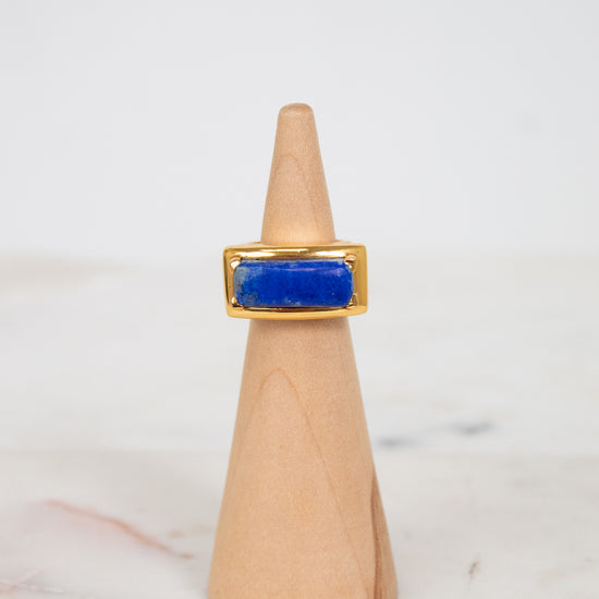 Gold ring with a blue stone on a wooden cone against a white background