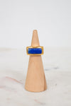 Gold ring with a blue stone on a wooden cone against a white background