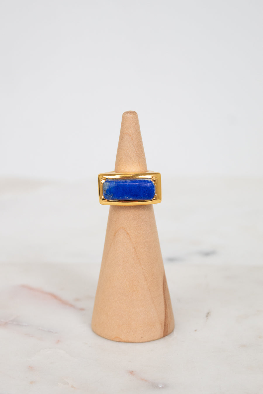 Gold ring with a blue stone on a wooden cone against a white background