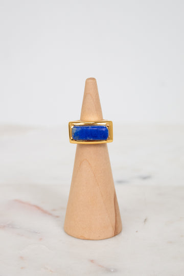 Gold ring with a blue stone on a wooden cone against a white background