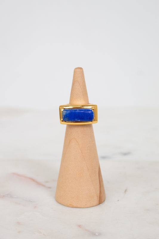 Gold ring with a blue stone on a wooden cone against a white background