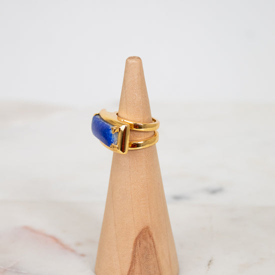 Gold ring with a blue stone on a wooden cone against a white background