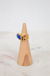 Gold ring with a blue stone on a wooden cone against a white background