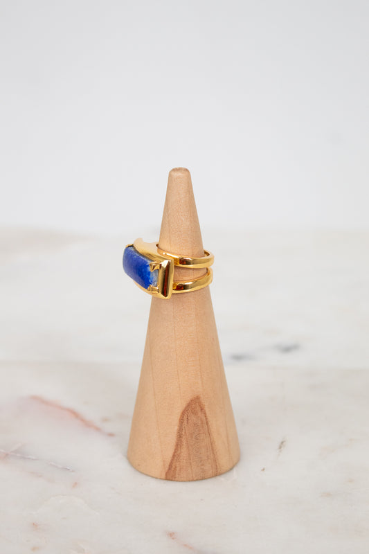 Gold ring with a blue stone on a wooden cone against a white background