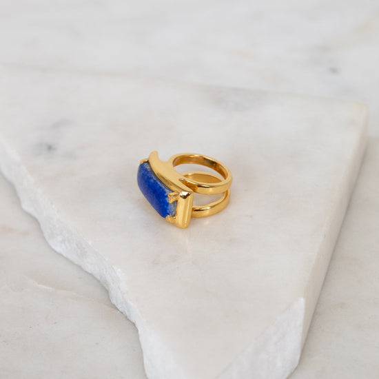 Gold ring with a blue stone on a marble surface