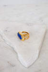 Gold ring with a blue stone on a marble surface
