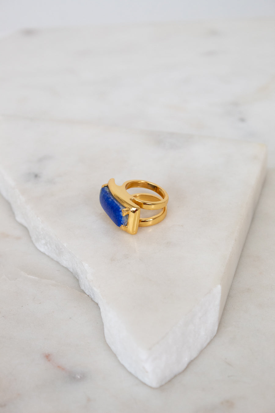 Gold ring with a blue stone on a marble surface