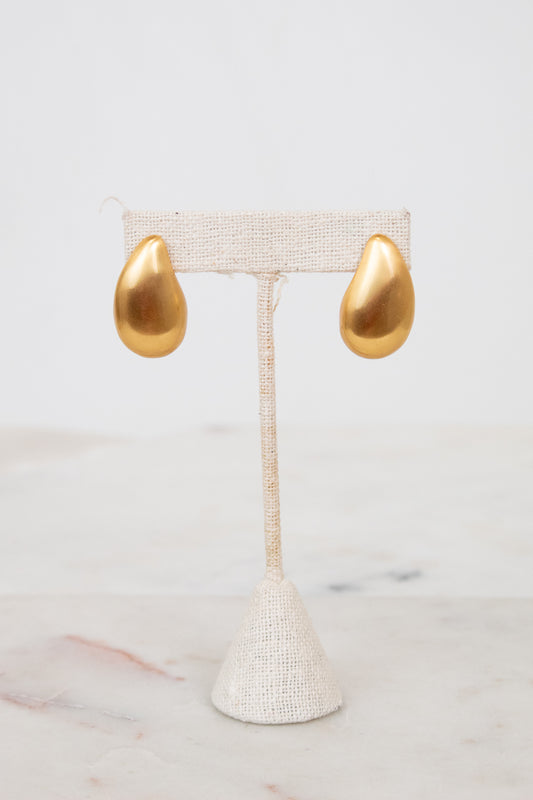 Gold teardrop earrings on a white earring stand with a marble background