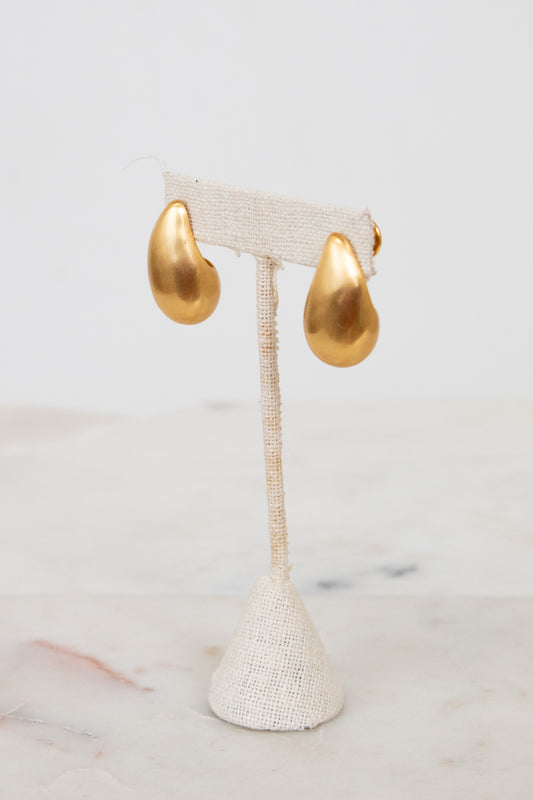 Gold teardrop earrings on a white earring stand with a marble background