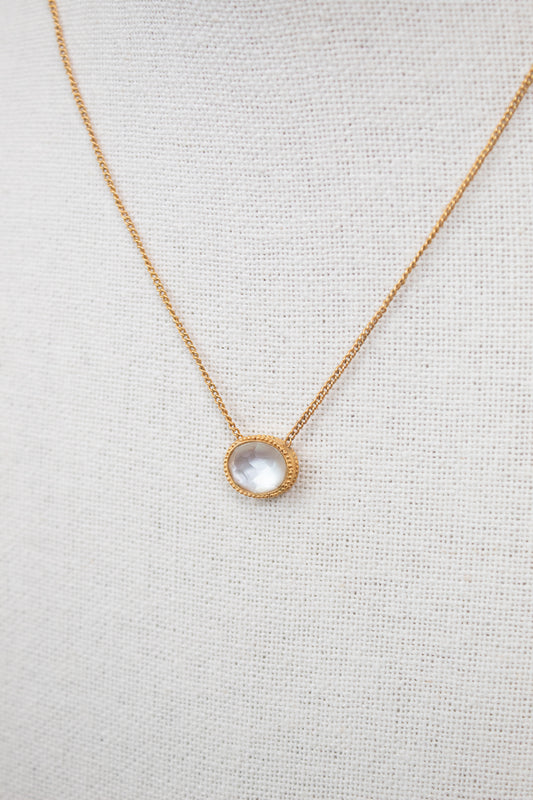 Close up of clear oval pendant on dainty gold chain against a plain background