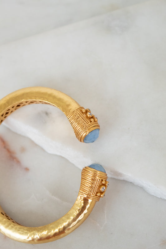 Gold bracelet with blue stones on a marble surface