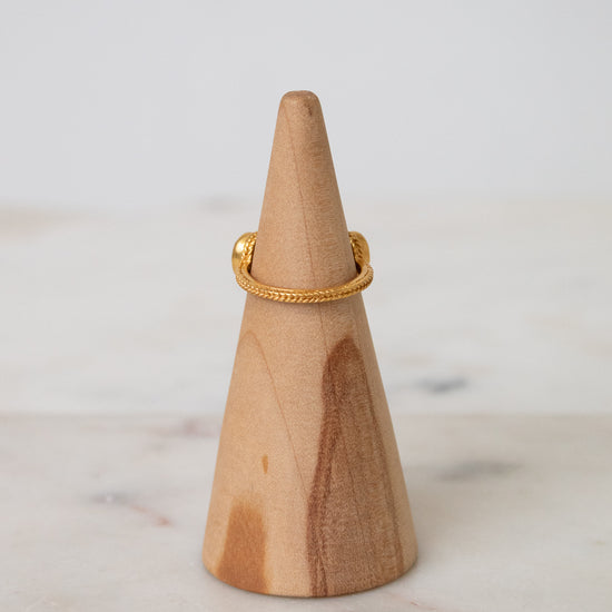 Back view of a delicate gold ring displayed on a light wood cone stand against a soft white background.