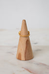 Back view of a delicate gold ring displayed on a light wood cone stand against a soft white background.