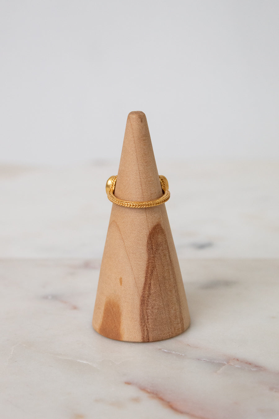 Back view of a delicate gold ring displayed on a light wood cone stand against a soft white background.