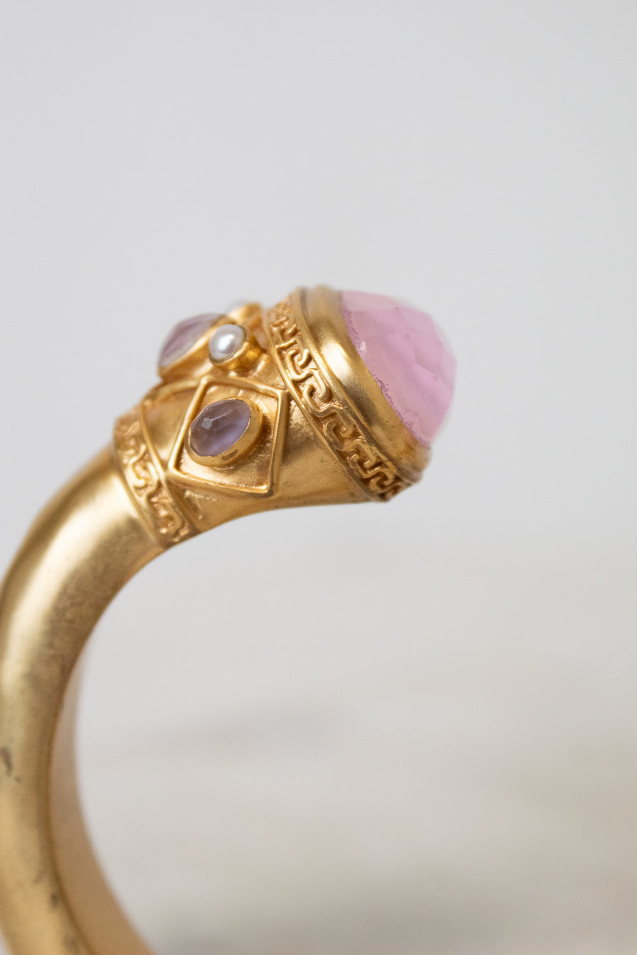 A close-up of a gold bracelet featuring a large pink cabochon stone and smaller purple and clear stones in an ornate setting.