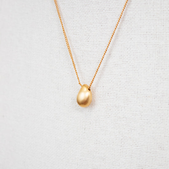 Gold necklace with a teardrop pendant on a light gray background