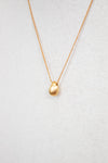 Gold necklace with a teardrop pendant on a light gray background