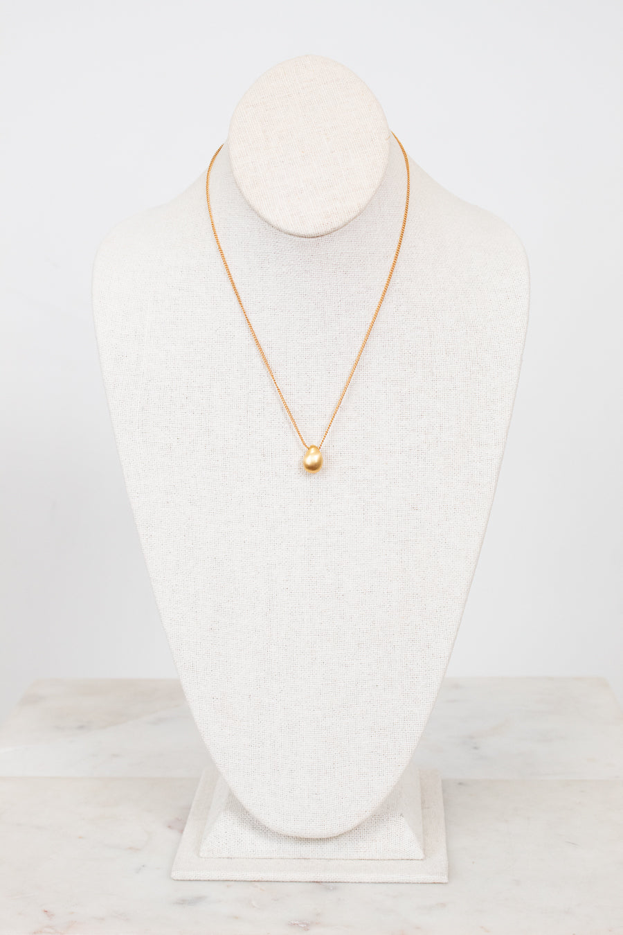 Gold necklace on a white mannequin bust against a white background