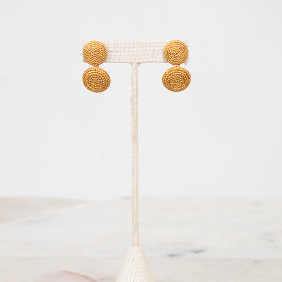 Gold circular earrings on a white stand with a white background