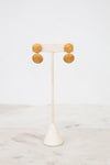 Gold circular earrings on a white stand with a white background