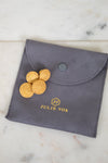 Gray pouch with gold coins and 'Julie Vos' branding on a marble surface