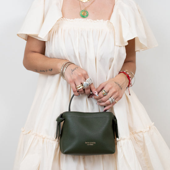Woman in a white dress holding a green handbag against a plain background