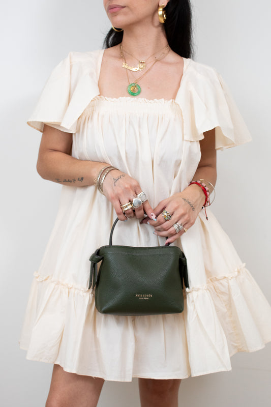 Woman in a white dress holding a green handbag against a plain background