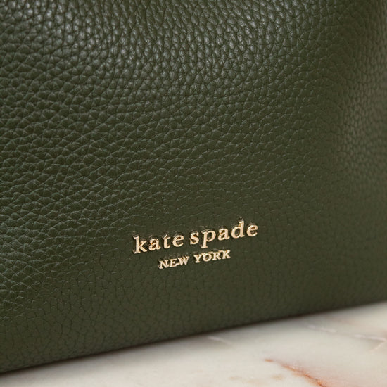 Green leather handbag with 'kate spade New York' logo on a marble surface