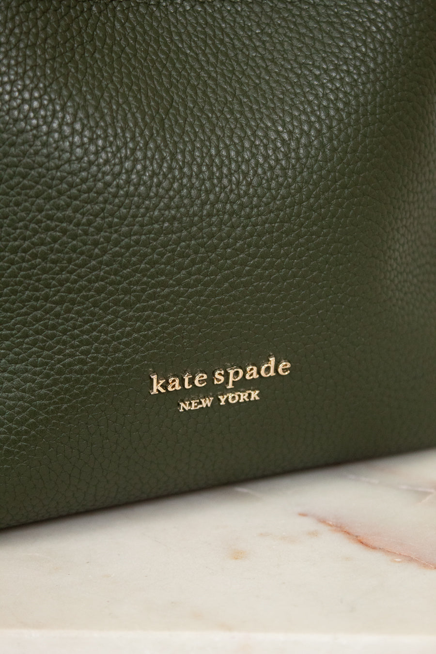 Green leather handbag with 'kate spade New York' logo on a marble surface