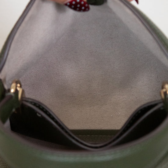 Close-up of a hand holding a green handbag with a blurred background