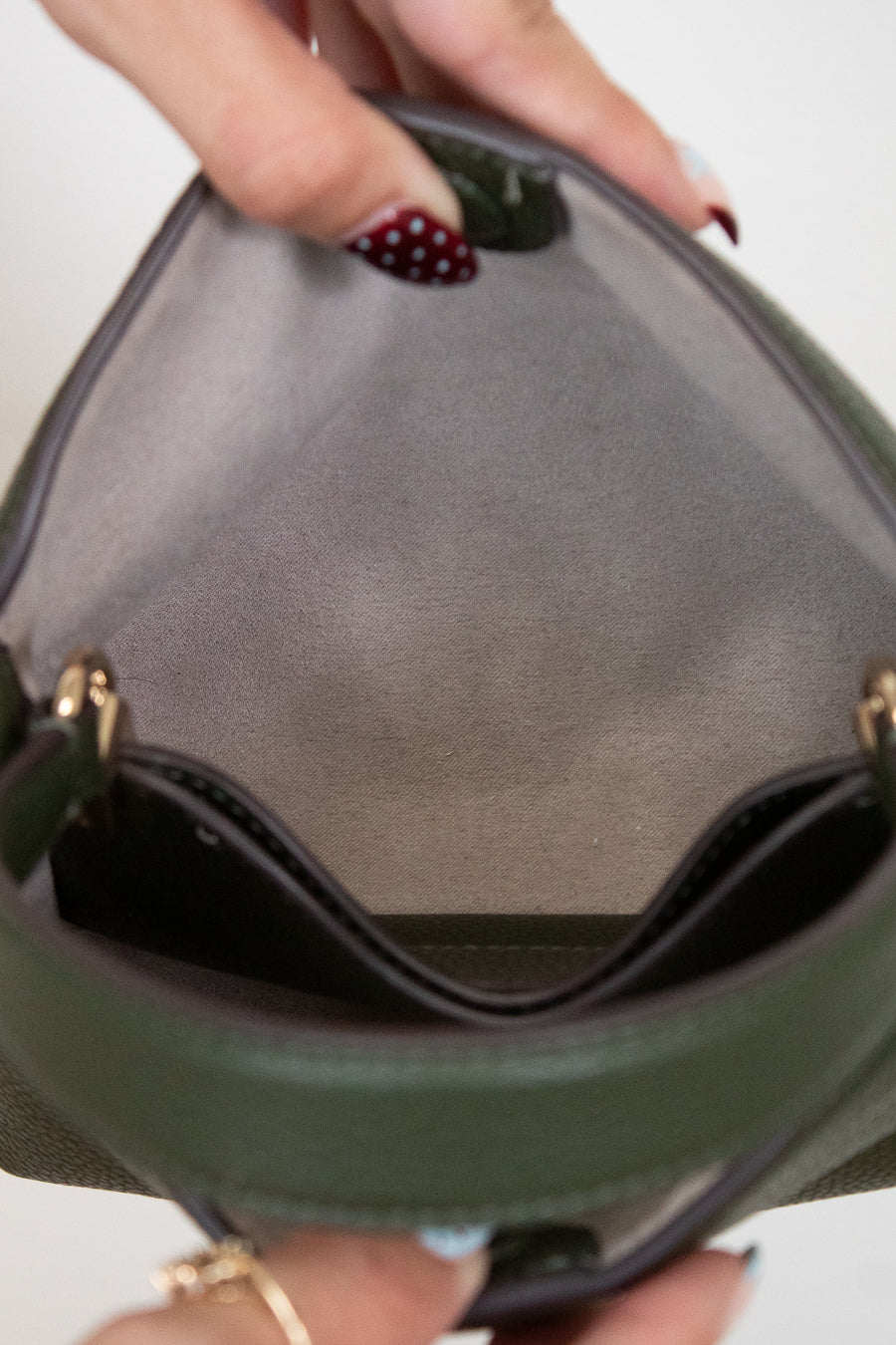 Close-up of a hand holding a green handbag with a blurred background