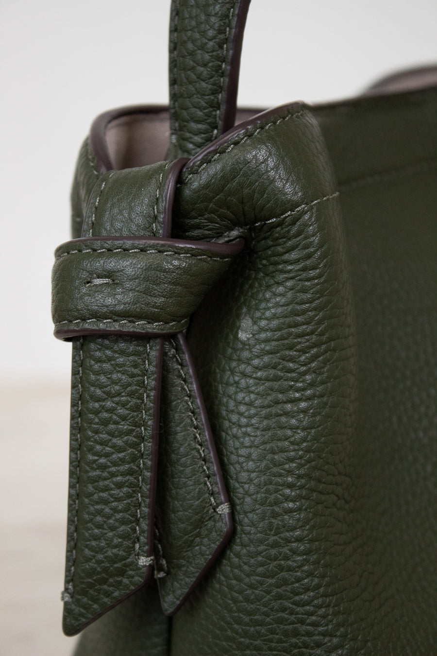 Close-up of a green leather handbag with a knot detail.