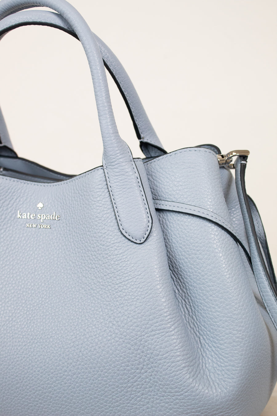 Light blue handbag with 'kate spade' logo on a beige background