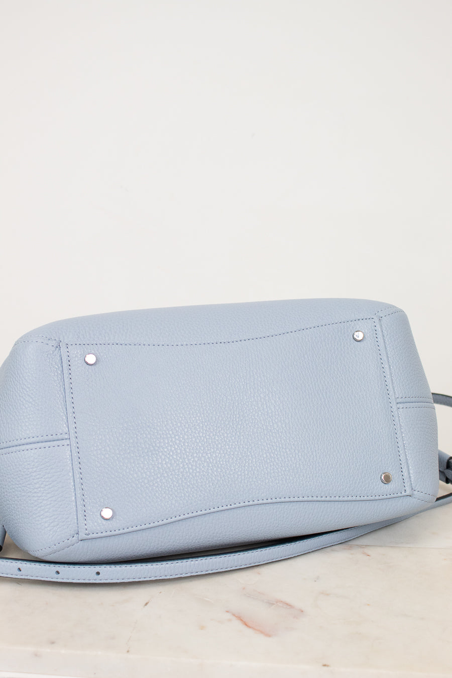Light blue handbag with silver studs on a light marble surface