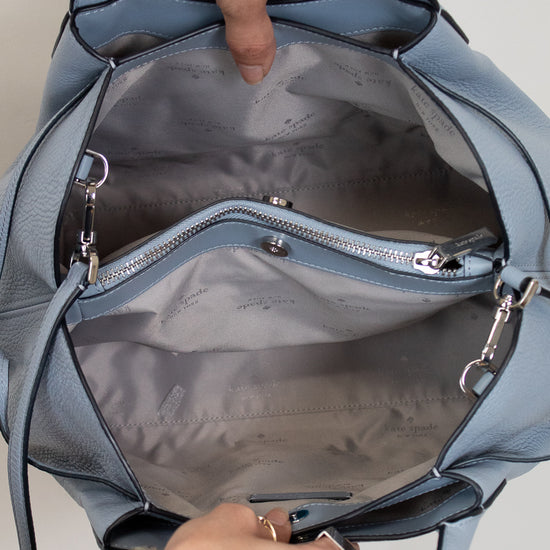 Blue handbag with a person's hands opening it, showing the interior.