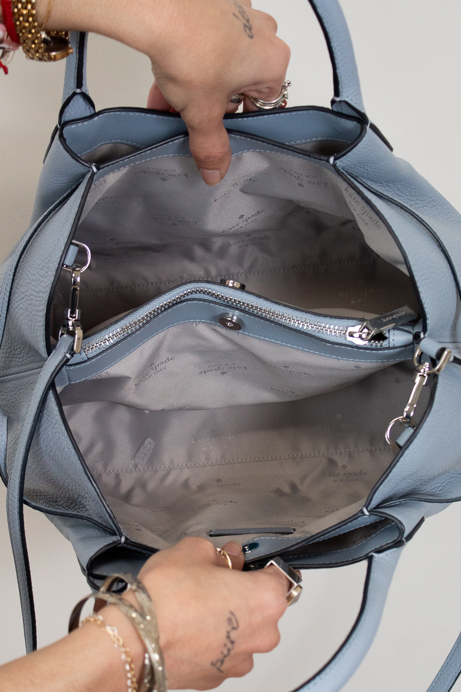 Blue handbag with a person's hands opening it, showing the interior.