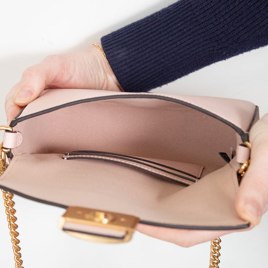 Person holding a pink handbag with gold chain strap on a white background