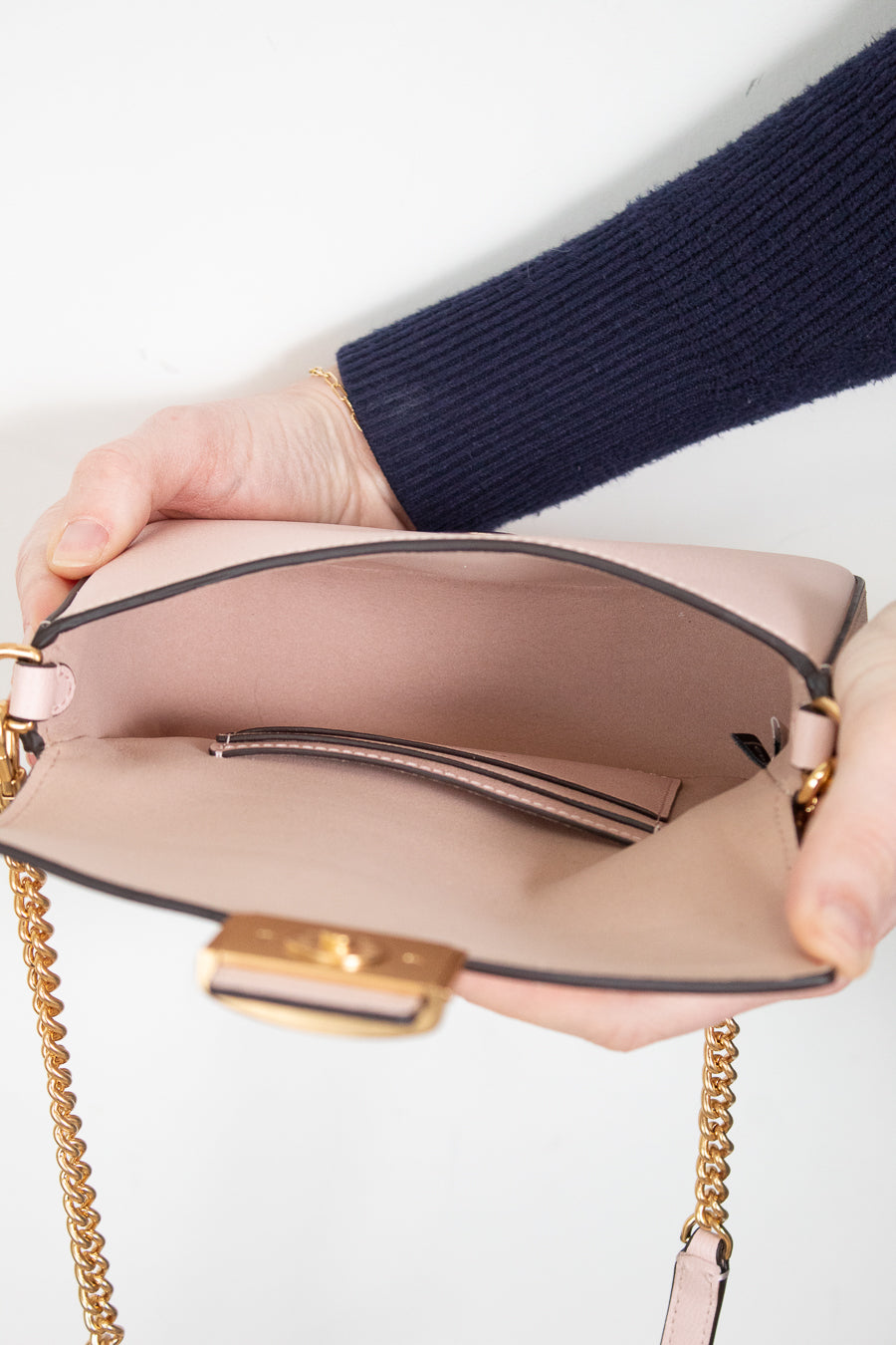Person holding a pink handbag with gold chain strap on a white background
