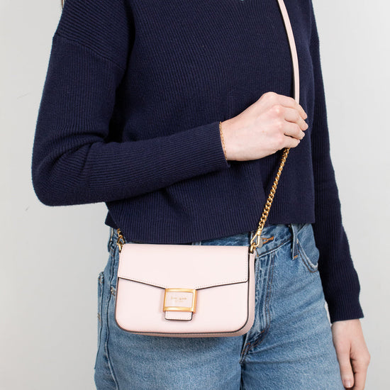 Person wearing a navy sweater and blue jeans with a blush pink handbag on a plain background