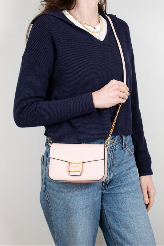 Person wearing a navy sweater and blue jeans with a blush pink handbag on a plain background