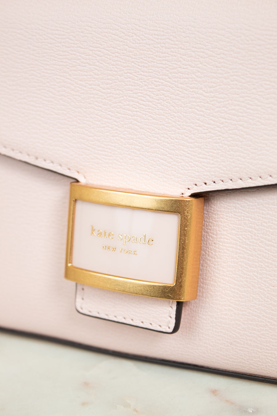 Close-up of a light pink handbag with a gold clasp and 'kate spade' label.
