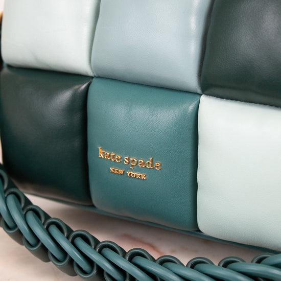 Close-up of a Kate Spade New York quilted leather handbag in shades of teal, dark forest green, and pale mint, featuring a braided shoulder strap and gold logo lettering.