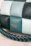 Close-up of a Kate Spade New York quilted leather handbag in shades of teal, dark forest green, and pale mint, featuring a braided shoulder strap and gold logo lettering.